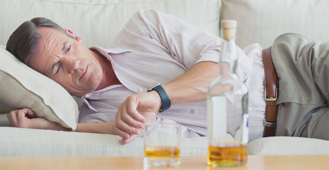 Мужчина лежит на диване и смотрит на часы