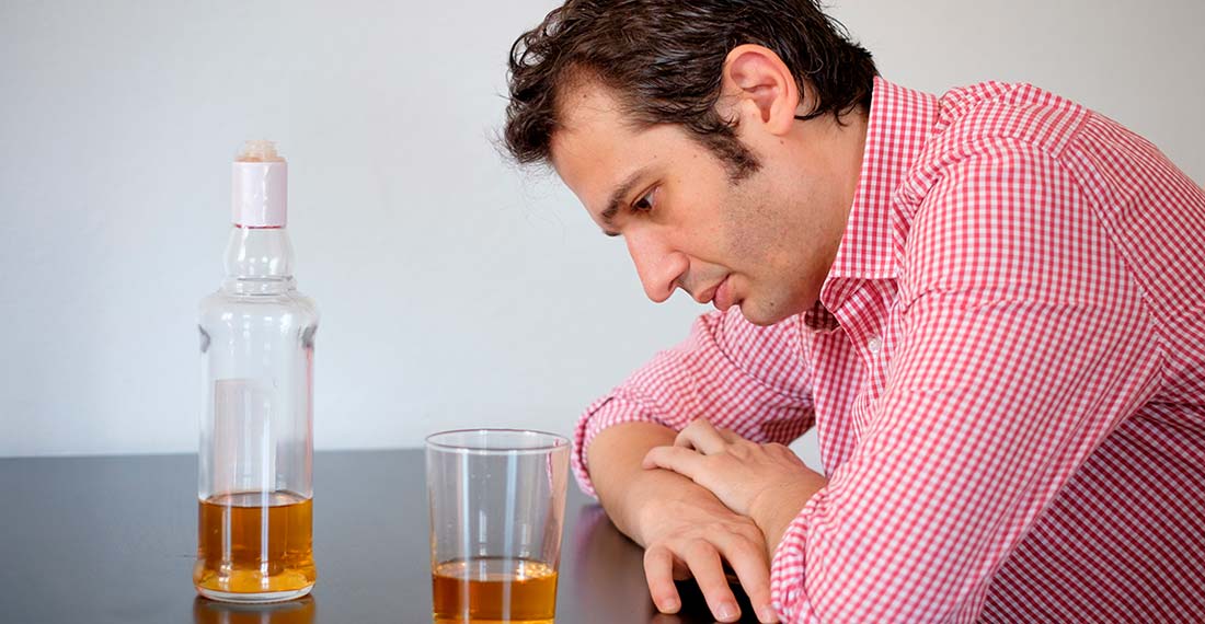 грустный мужчина сидит за столом с алкоголем